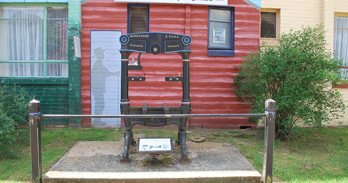 The printing press from the defunct Jamieson Chronicle newspaper. It is mounted in front of a mural painted on the wall of the Courthouse Hotel showing the old newspaper building - in Jamieson, Victoria